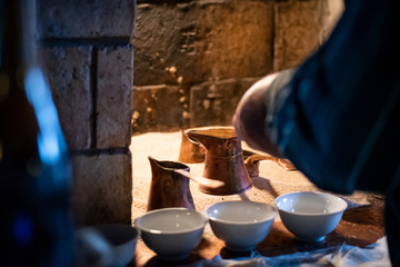 Man pouring Turkish coffee from a traditional brass pot, prepared on hot sand in an oven