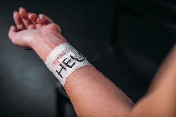 partial view of woman showing hand with word help on medical patches fixed on cut wrist on black background