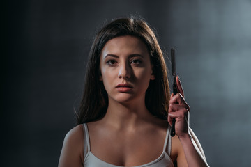 depressed young woman looking at camera while holding straight razor on dark background