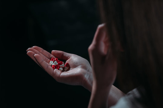 partial view of woman going to commit suicide and holding handful of pills isolated on black isolated on black