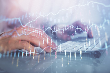 Double exposure of graph with man typing on computer in office on background. Concept of hard work.