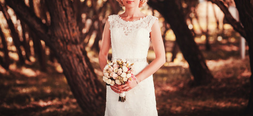 bride in a white dress holding a bouquet of flowers on the background of green grass
