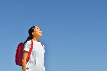 青空で見上げる小学生の女の子（ランドセル）