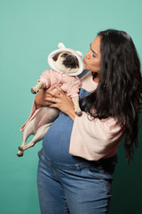 Pregnant brunette kisses pug on empty blue background