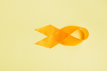 top view of yellow awareness ribbon on yellow background, suicide prevention concept