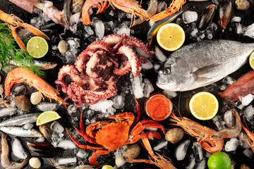 Fish and seafood variety, a flat lay top shot on a black background. Sea bream. shrimps, crab, sardines, squid, mussels, octopus and other fresh products