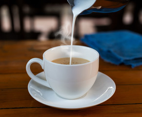 Pour the milk into the coffee in a white cup