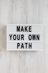 'Make your own path' words on a modern board, clipboard with blank sheet of paper on a white wooden surface, top view. Overhead, from above, flat lay.