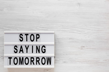 'Stop saying tomorrow' words on a lightbox on a white wooden surface, top view. Overhead, from above, flat lay. Space for text.