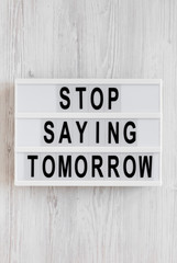 'Stop saying tomorrow' words on a modern board on a white wooden background, top view. Overhead, from above, flat lay.