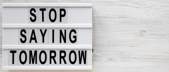 'Stop saying tomorrow' words on a modern board on a white wooden surface, top view. Overhead, from above, flat lay. Copy space.