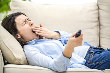 Crop. Bored and relaxed woman is watching TV, laying on a sofa and yawning. Close up.