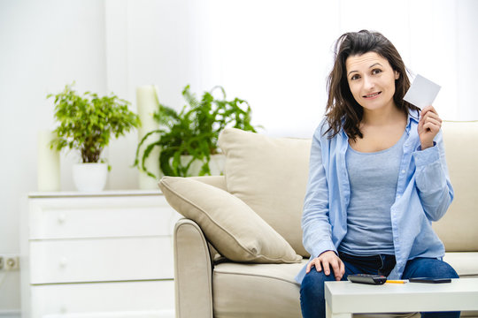 Attractive brunette woman is showing white paper sticket and smiles slightly. Copy space.