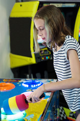 Little girl playing hammer arcade game machine in theme park.