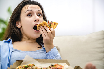 Amazed woman with risen eyebrows bites a slice of pizza. Close up.