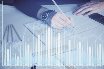 Double exposure of man's hands writing notes of stock market with forex chart.