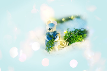 A white rat made of wool carries a Christmas tree among abstract bright light festive background.