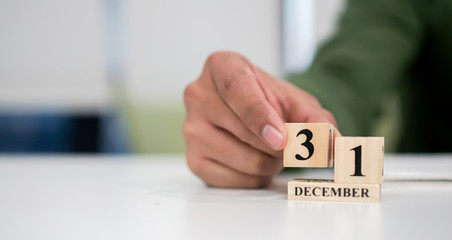 close up employee man hand put number _ of cube shape wood to make calendar date December 31 at...
