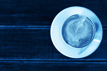 Color of year, 2020. Cup of cappuccino or latte on wooden background, toned classic blue photo. Coffee cup, top view.