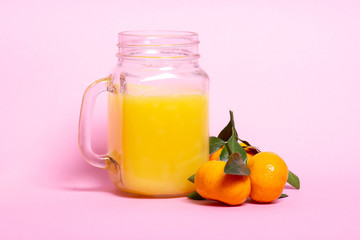 Citrus juice in a jar with a pen and fresh orange mandarin on a pink background