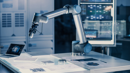 Futuristic Artificial Intelligence Robotic Arm Operates and Moves a Metal Object, Picks It Up and Puts it Down. Scene is Taken in a High Tech Research Laboratory with Modern Equipment.