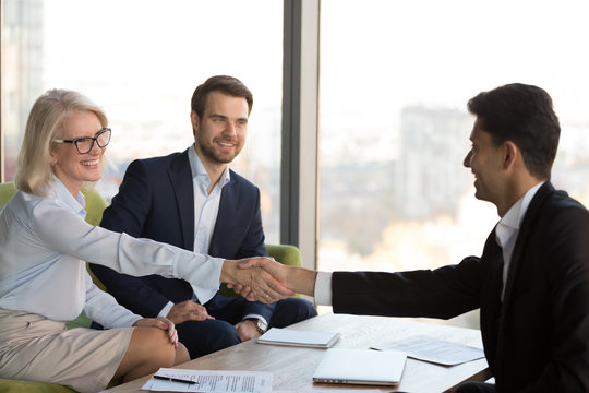 Smiling mature businesswoman shaking hand of business partner at meeting