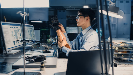 Futuristic Prosthetic Robot Arm Being Tested by a Professional Japanese Development Engineer in a High Tech Research Laboratory with Modern Computer Equipment. He is Satidfied with the Result.