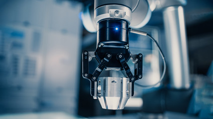 Close Up of a Futuristic Robotic Arm Moving a Metal Object and Placing It. Team of Engineers Observe This Advanced Process. They are in a High Tech Research Laboratory with Modern Equipment.