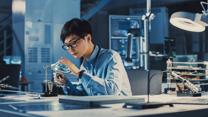 Professional Japanese Electronics Development Engineer in Blue Shirt is Soldering a Circuit Board in a High Tech Research Laboratory with Modern Computer Equipment.