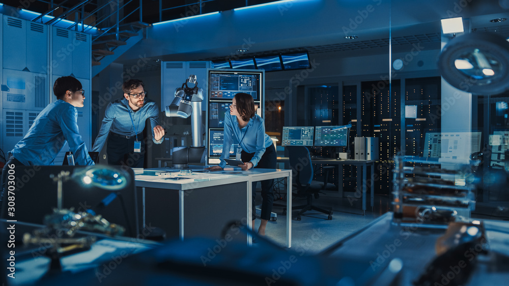 Leinwandbilder Futuristic Metal Robotic Arm is Moving a Metal Object. Senior Engineer Talks Through This Advanced Process with His Diverse Team. They are in a High Tech Research Laboratory with Modern Equipment.