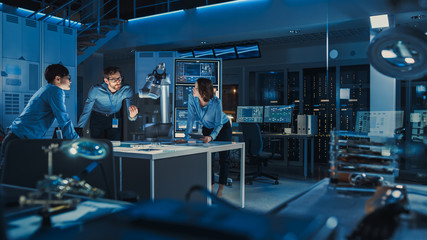 Futuristic Metal Robotic Arm is Moving a Metal Object. Senior Engineer Talks Through This Advanced Process with His Diverse Team. They are in a High Tech Research Laboratory with Modern Equipment.