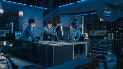 Futuristic Robotic Arm is Moving and Placing a Metal Object. Senior Engineer Talks Through This Advanced Process with His Diverse Team. They are in High Tech Research Laboratory with Modern Equipment