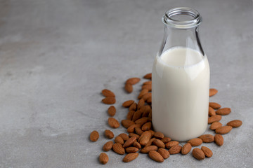 Almond drink milk in glass bottle surrounded by almonds nuts