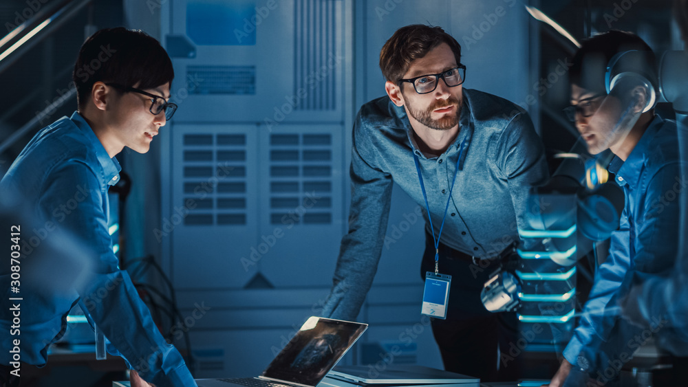 Fototapete diverse team of engineers with laptop and a tablet analyse and discuss how a futuristic robotic arm 