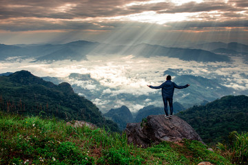 Man stands on the peak of sandstone rock and watching to Sun. Beautiful moment the miracle of nature. Misty valley.Foggy mountains
