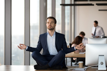 Calm businessman meditating on office desk, stress relief concept