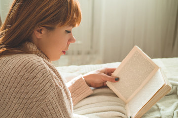 Attractive young woman is reading a book at home. Thoughtful girl reading important book.