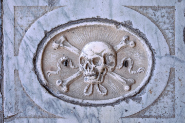 Classical skull with crossed bones symbol carved in marble stone on italian tomb. Antique medieval Crypt.  Old skull pattern, Memento mori. Retro design.