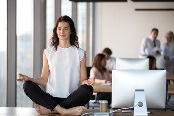Calm businesswoman with closed eyes meditating on office desk