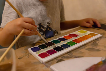 Children's hand brush with a wooden handle draws colorful watercolor paints in children's art school.