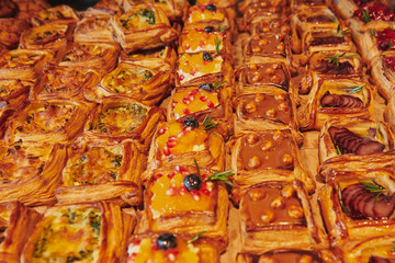 A lot of different puff pastry dessert with filling on the store counter. Caramel with nuts, fruits, berries and cheese with spinach.