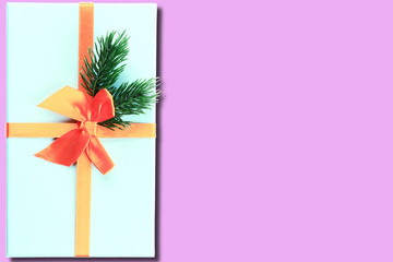 Christmas gift box blue. Pink background. Place for your text. Orange ribbon. Spruce branch. Shadow. Top view.