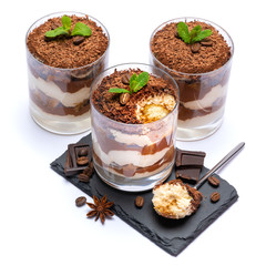 Classic tiramisu dessert in a glass cup on stone serving board and pieces of chocolate on white background with clipping path