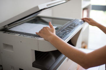 Close-up on the hands of a woman doing photocopies in the office. Woman making photocopy using copier in office. Female secretary making photocopies on machine in office.