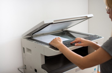 Close-up on the hands of a woman doing photocopies in the office. Woman making photocopy using copier in office. Female secretary making photocopies on machine in office.