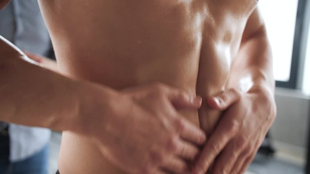 Athletic man putting oil on abs and preparing for workout
