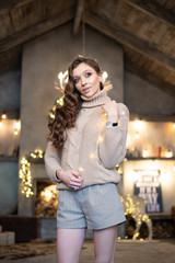 Beautiful woman (girl) with long hair dressed in a warm fashion long sleeve sweater among Christmas or New Year lights
