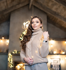 Beautiful woman (girl) with long hair dressed in a warm fashion long sleeve sweater among Christmas or New Year lights