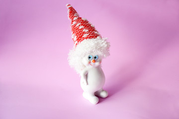 Funny and cute white snowman in a red hat with blue eyes on a delicate pink background. Christmas and New Year concept.