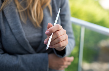 Female Business Leader holding a silver pen. Beautiful young woman in smart casual wear holding a pen standing against green background. Home broker standing on the taras of modern property.